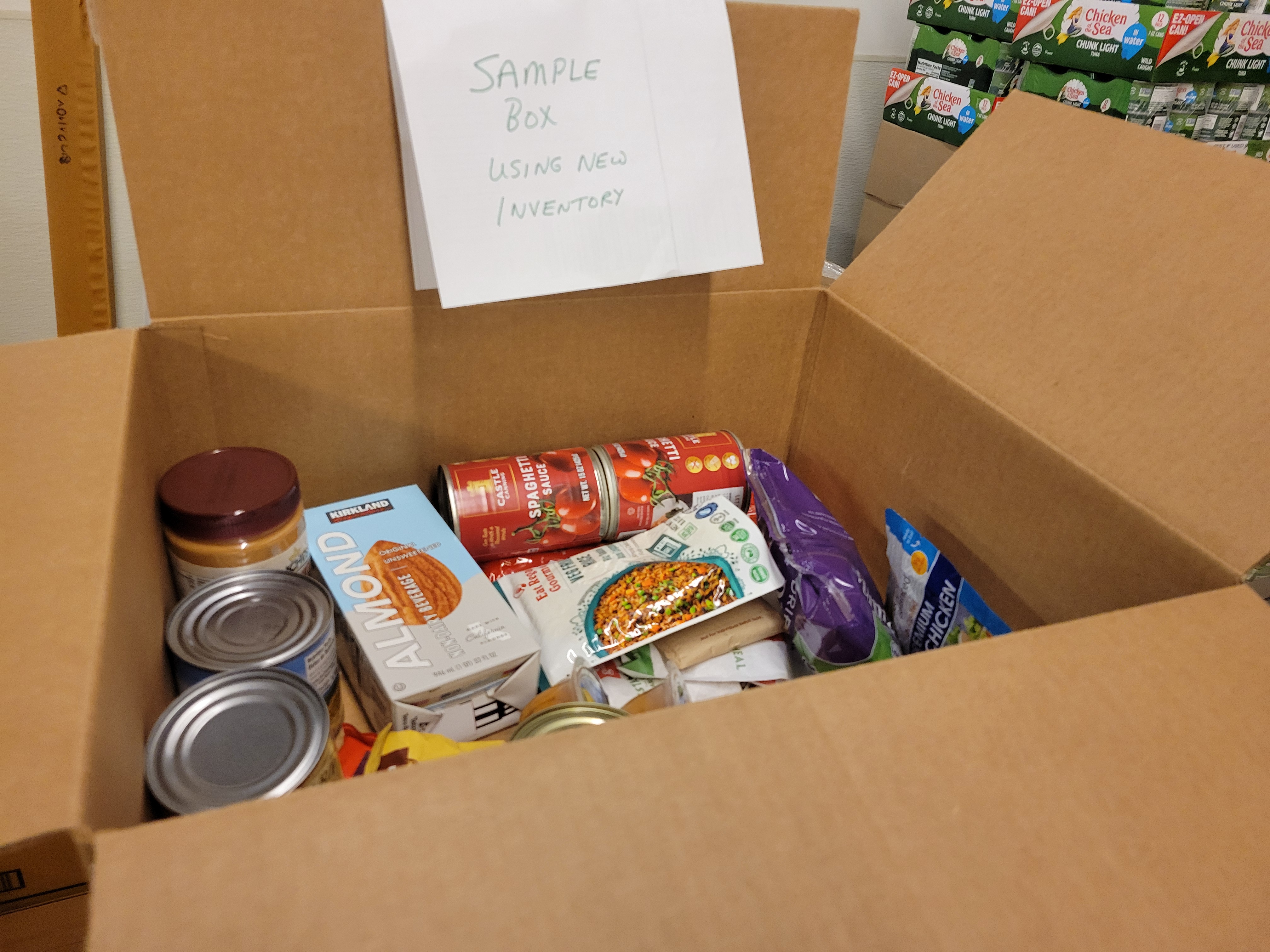 Cardboard box full of dry goods and a piece of paper listing sample box using new inventory.